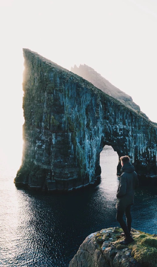 Someone standing on a cliff overlooking some water and more cliffs.