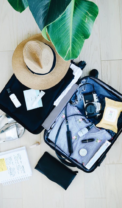 A suitcase full of clothing and vacation items, such as a hat and a camera.
