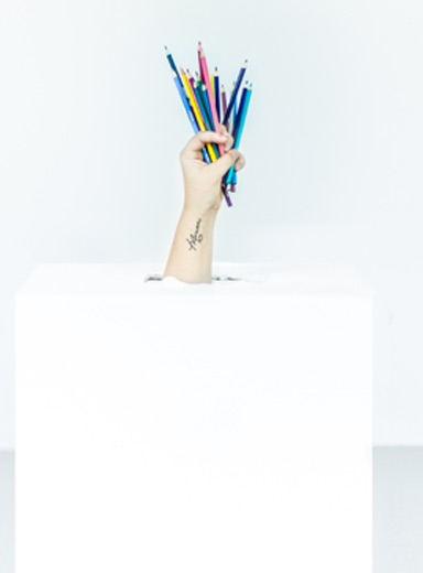 A hand holding pencil crayons coming out of a box. 