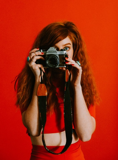 A woman holding a film camera on a red background.